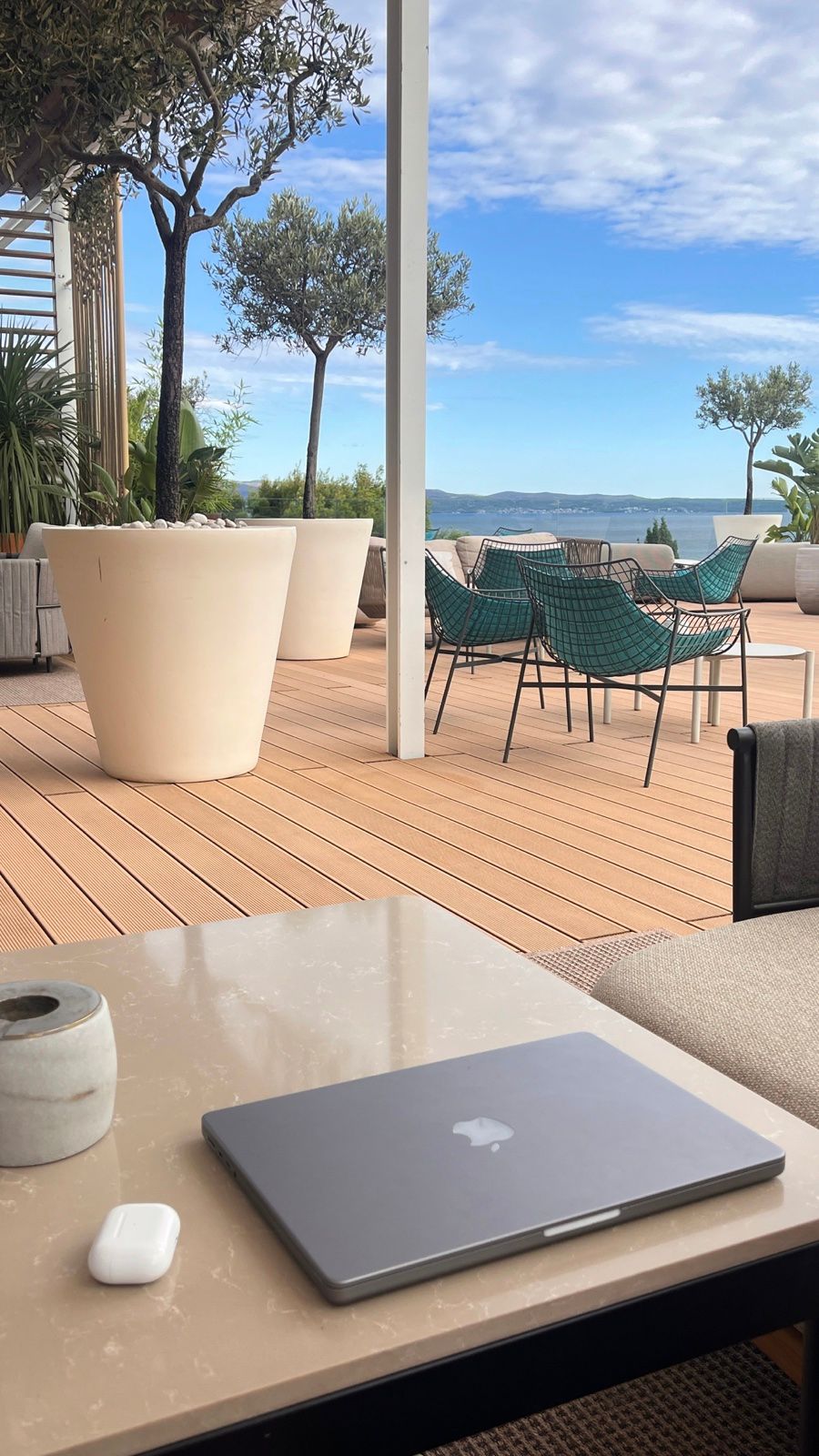 A laptop on a sunny terrace table looking out over the sea