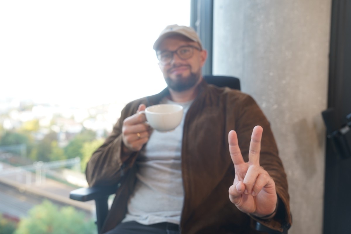 Team member with a coffee, waving at the camera